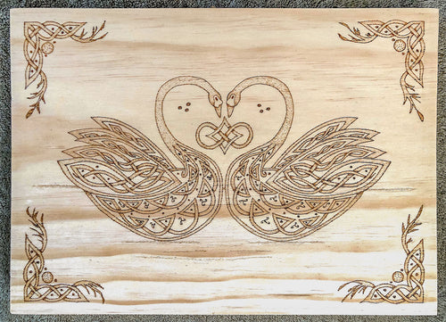 Wooden plaque with intricate Celtic knot design of two swans forming a heart shape.