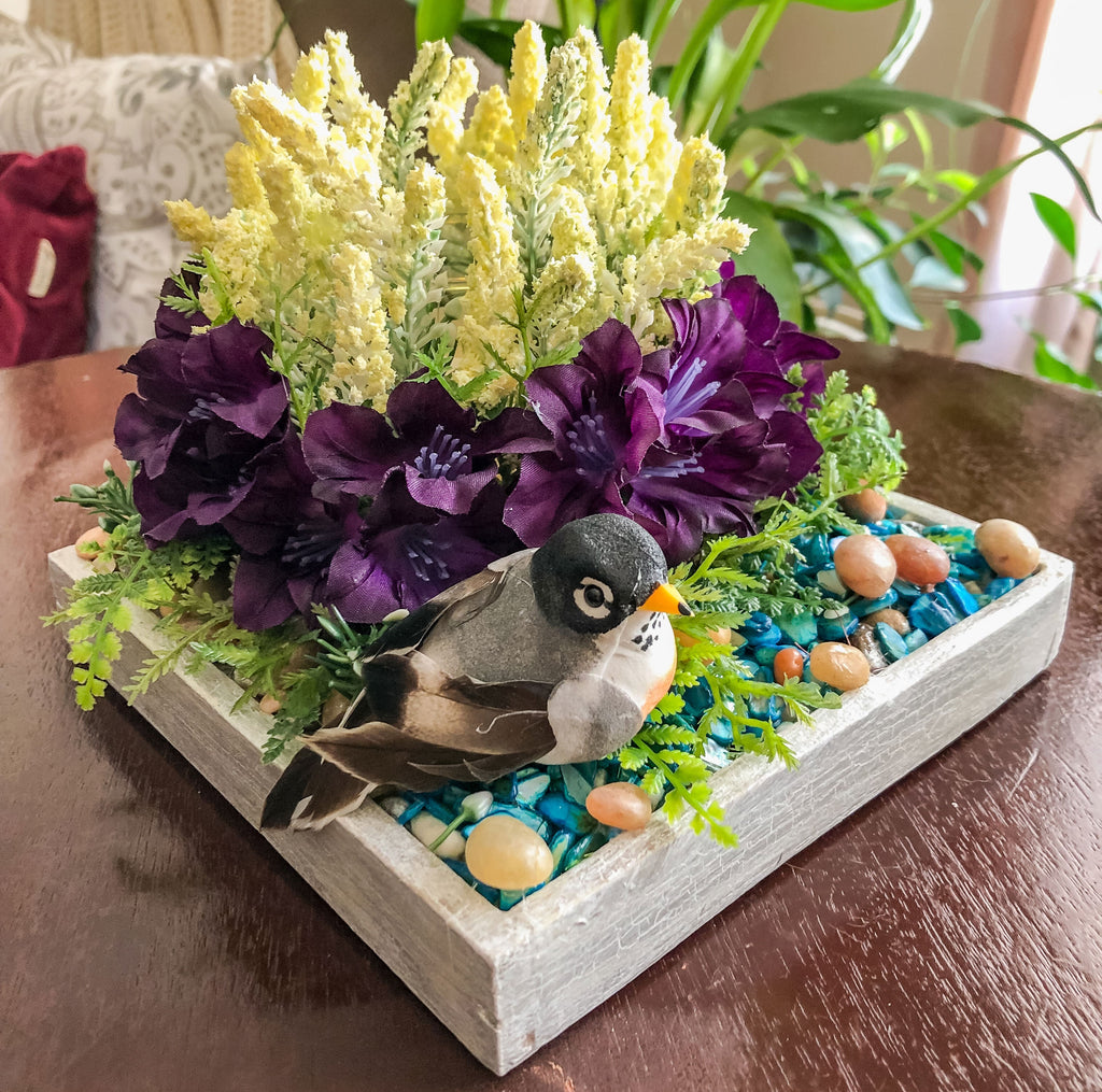 Candleholder with faux white and purple flowers and a mini bird on a table