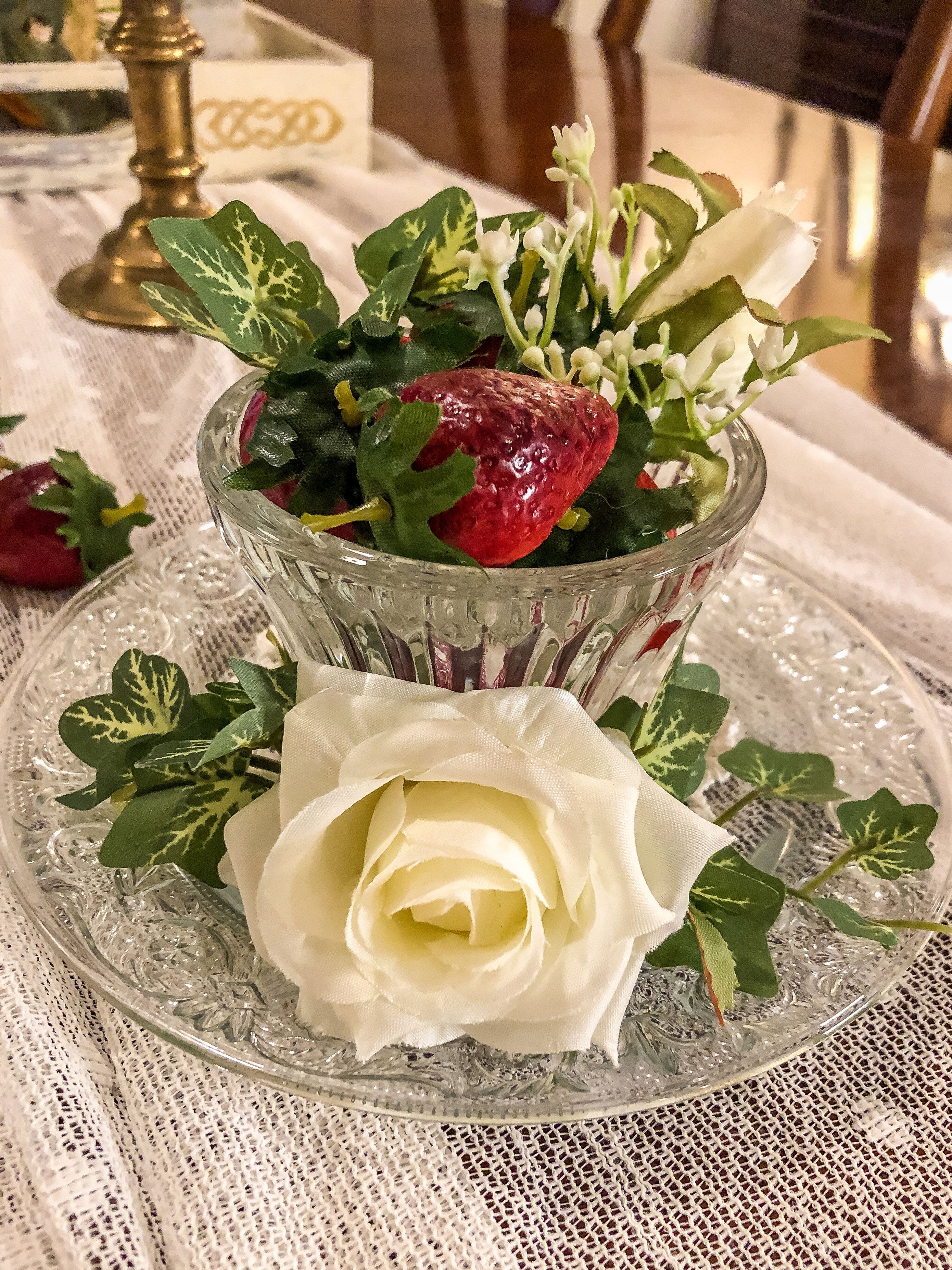 Artificial strawberries with white roses and ivy in a glass cup on a glass plate 