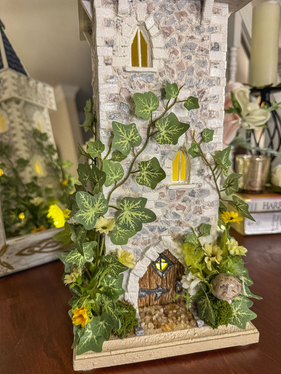 Decorative stone tower with ivy and flowers lit with fairy lights on a table