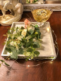 Fake champagne in a glass with faux florals and succulents on a tray with fairy lights
