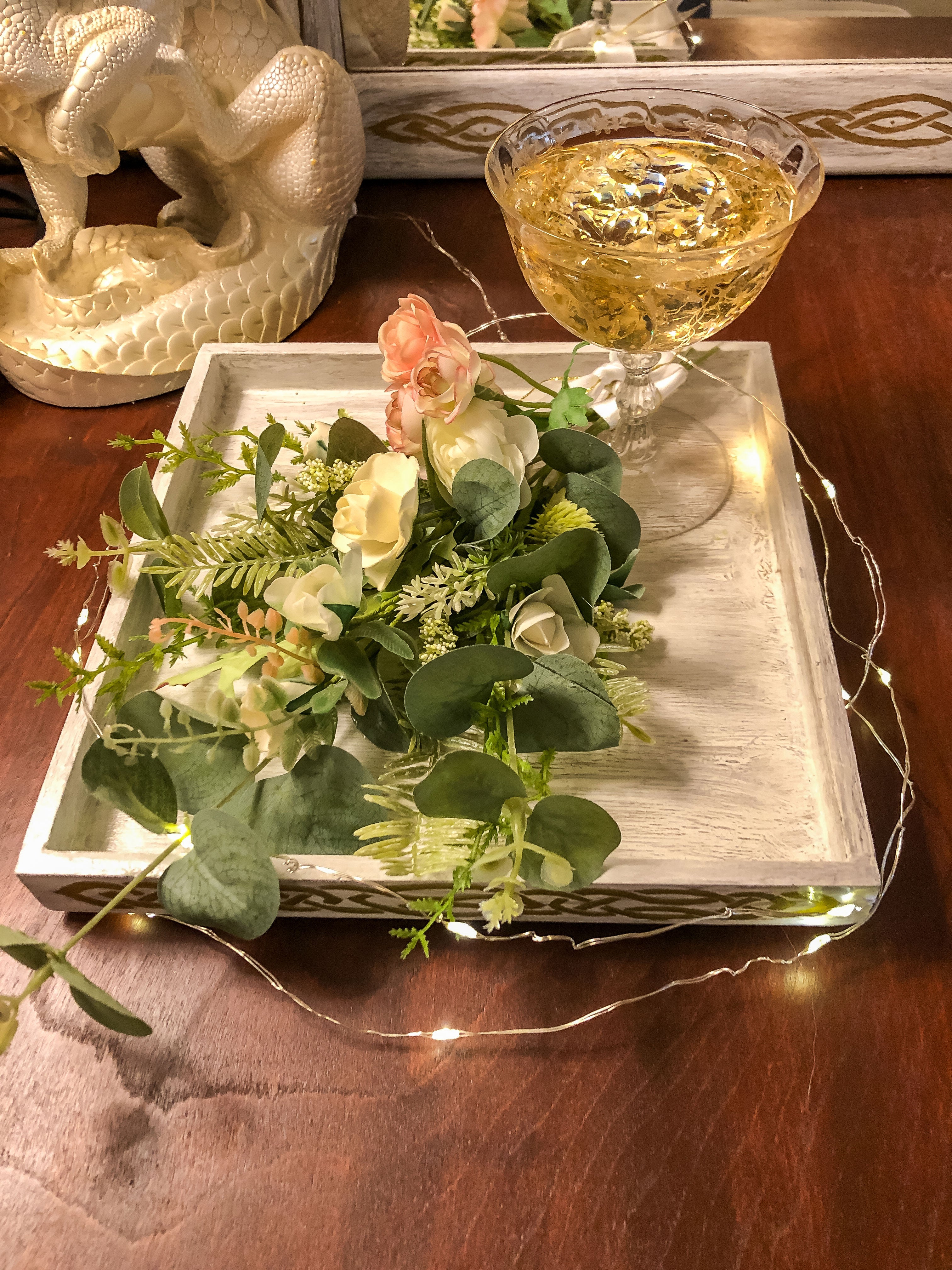 Fake champagne in a glass with faux florals and succulents on a tray with fairy lights