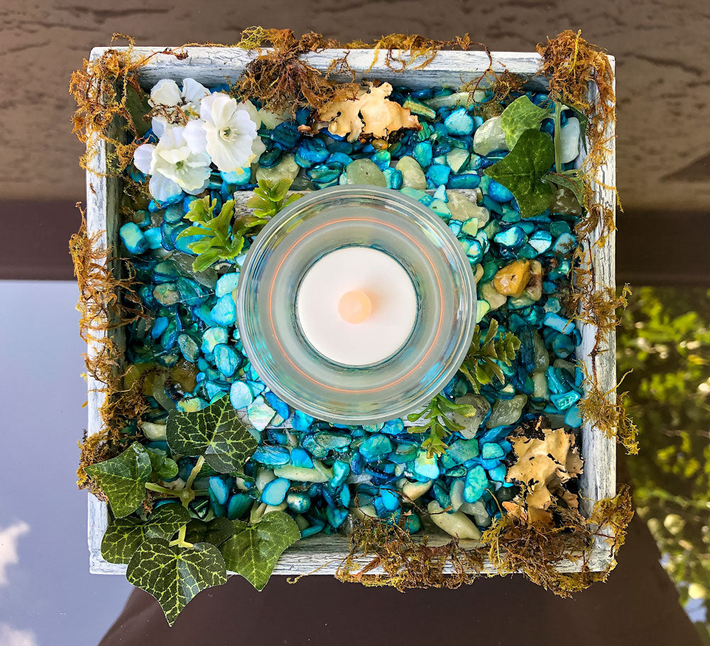 Votive candle holder with blue rocks and moss on a glass table