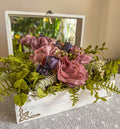 Artificial purple flower arrangement in a decorative wooden box with a mirror