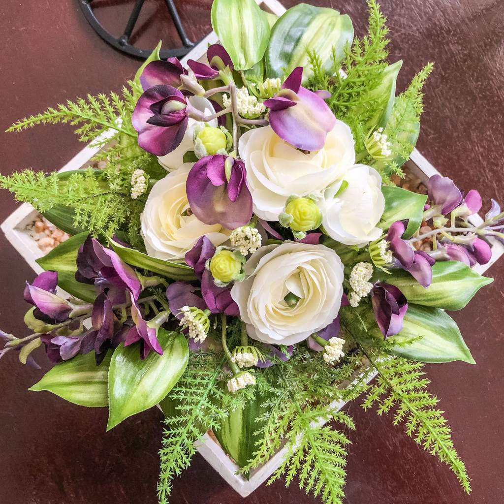 Artificial purple and white flowers with ferns in a tray on a table