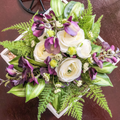 Artificial purple and white flowers with ferns in a tray on a table