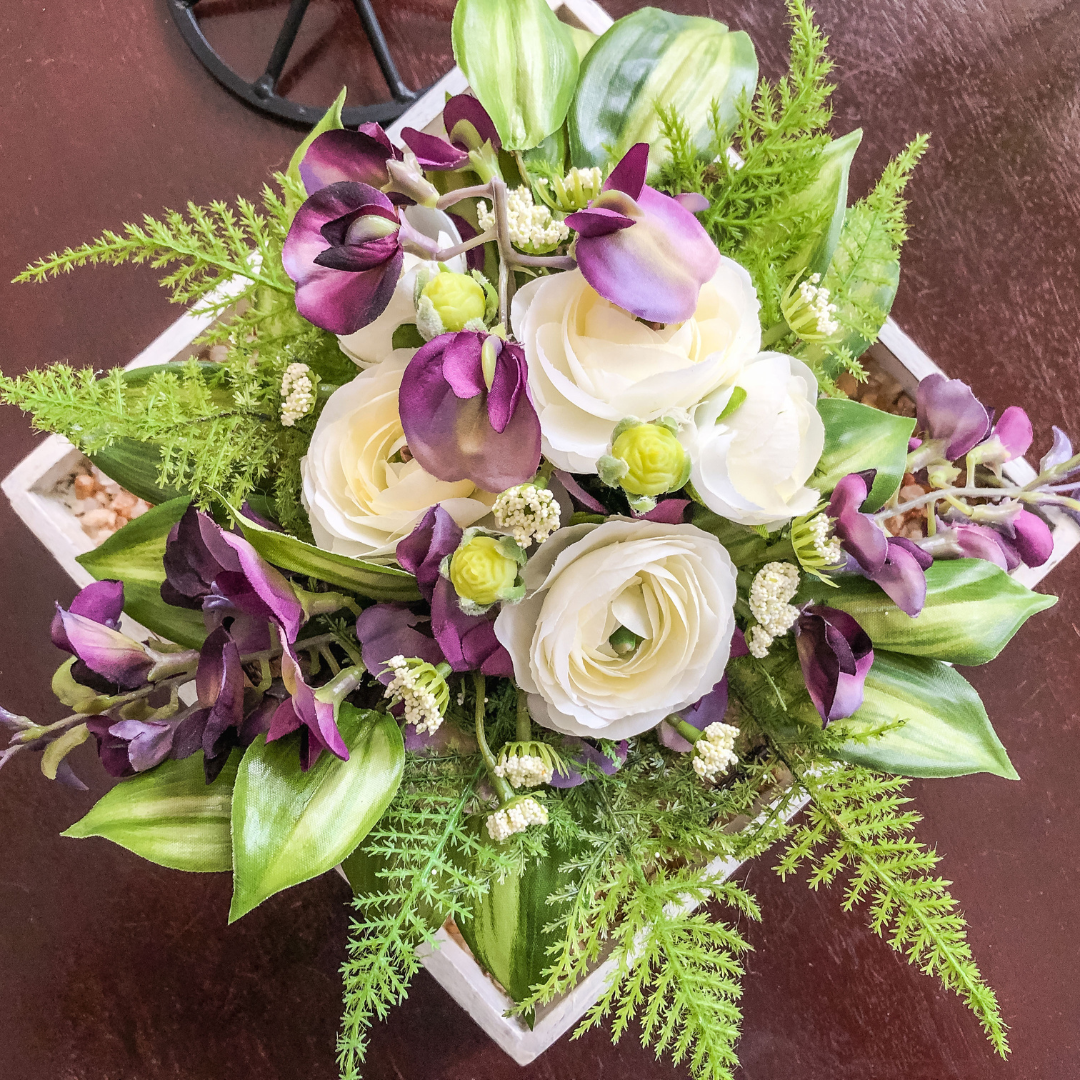 Artificial purple and white flowers with ferns in a tray on a table