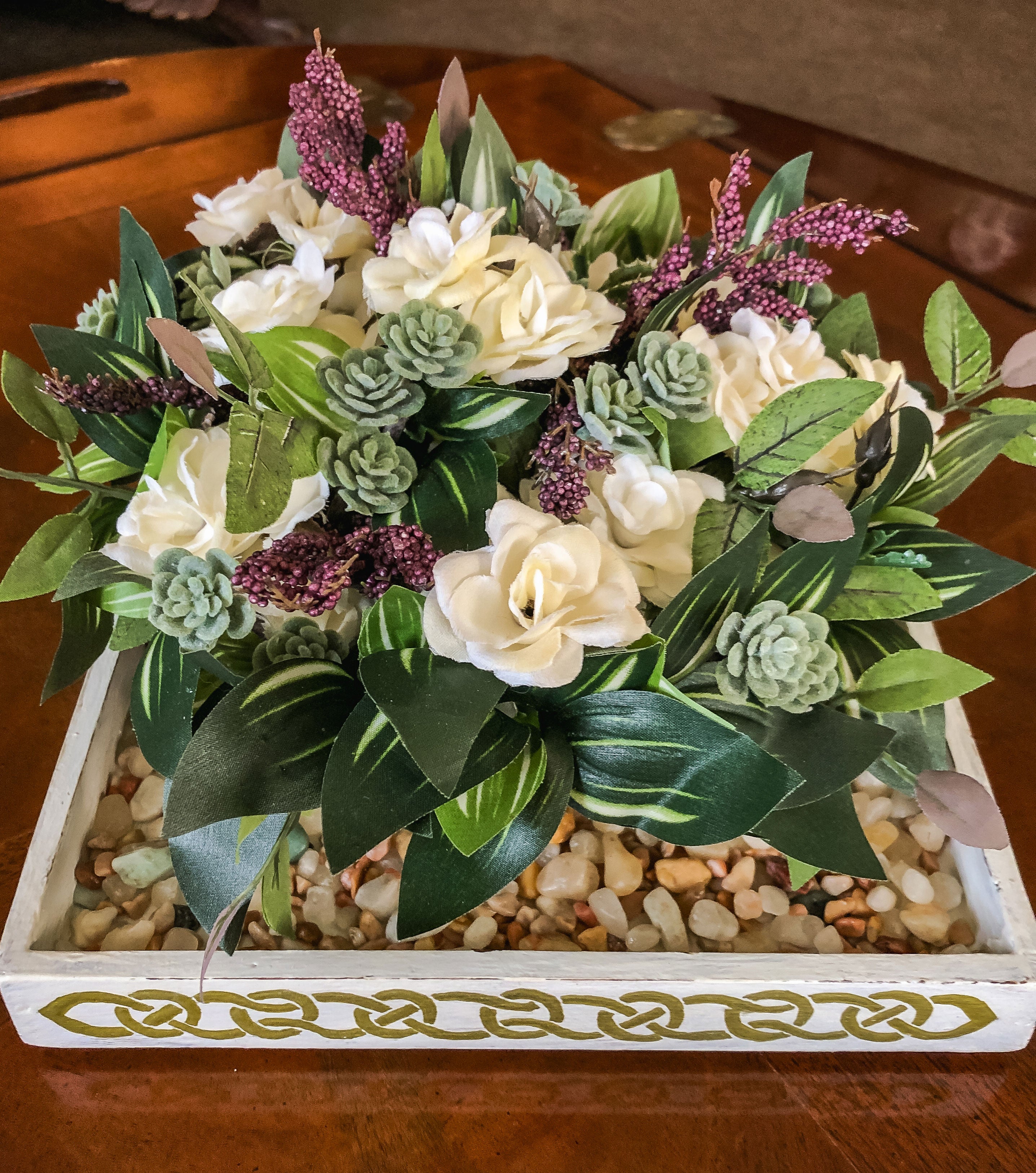 Faux floral arrangement with purple and white flowers and succulents in a gravel filled tray on a table