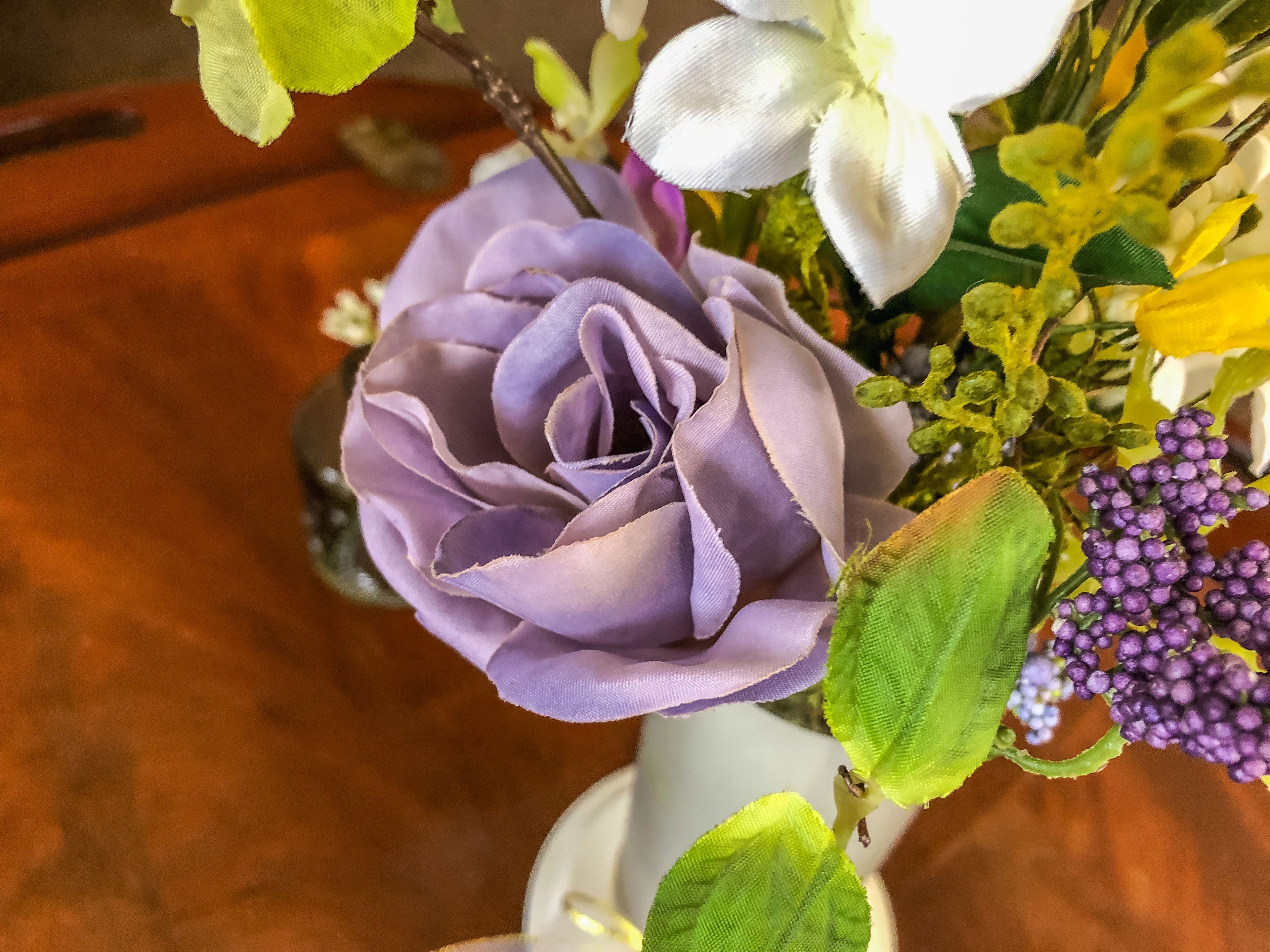 Purple fabric rose flower arrangement in a frosted glass