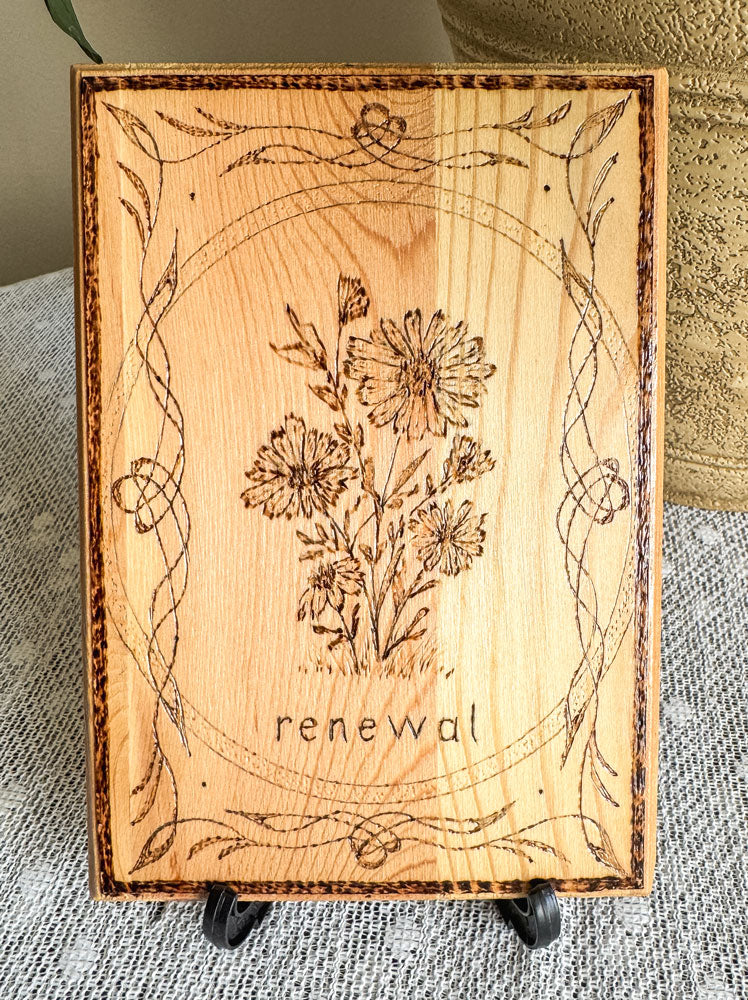 Small wood plaque with daisies and the word renewal on a stand