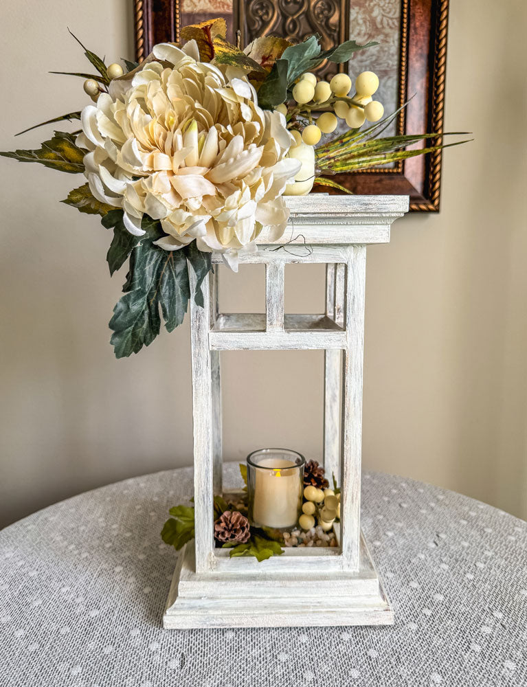 Decorative white lantern candleholder with faux flowers on a lace table