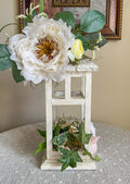 White lantern candleholder with faux summer florals on a lace table